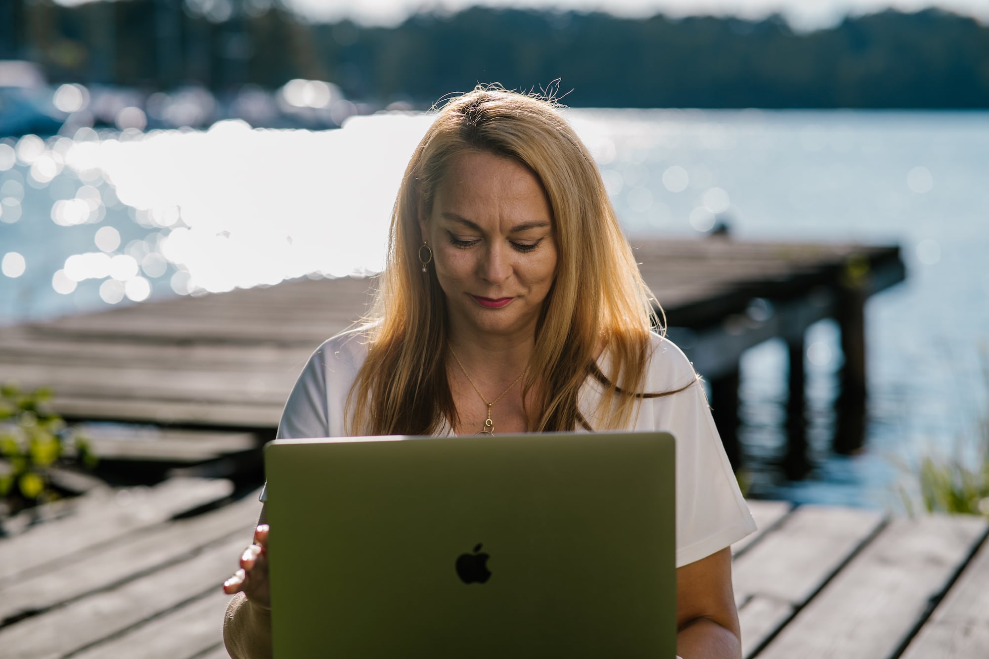 Kobieta siedząca na drewnianym pomoście z laptopem. W tle widać jezioro.